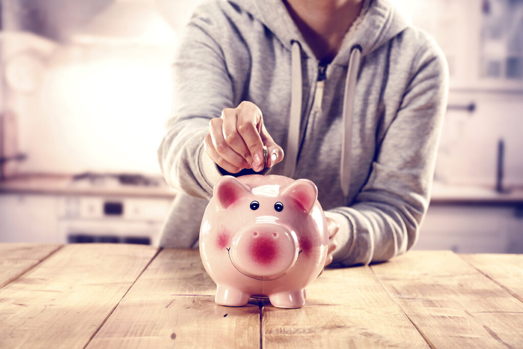 Person in gray jacket putting money into a piggy bank.