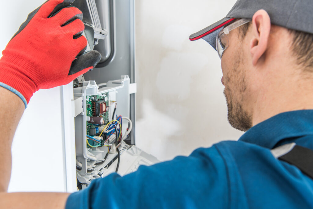 Technician repairing a residential furnace while wearing red work gloves.