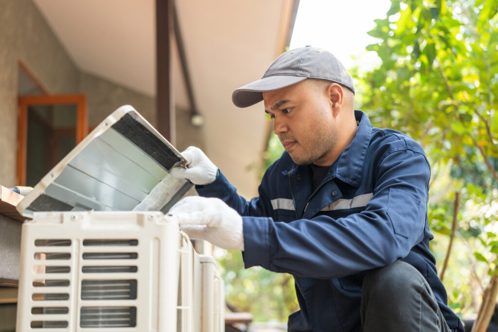 Technician servicing an outdoor heat pump unit next to a home.