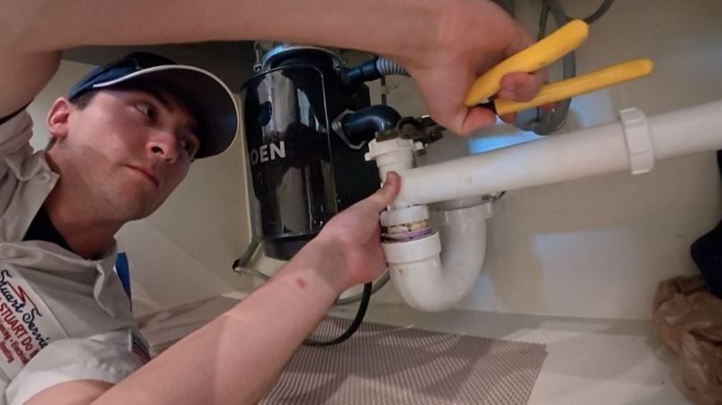 Plumber working on a garbage disposal under and sink.