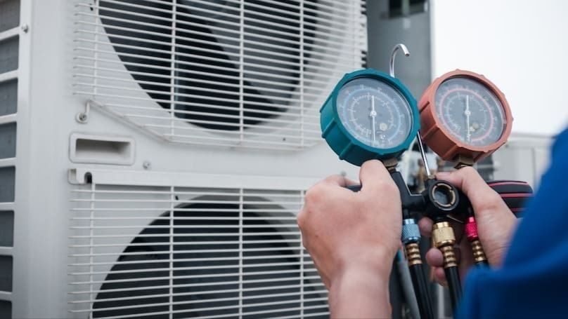 HVAC technician uses manifold gauge set to check refrigerant pressure on an outdoor air conditioner unit