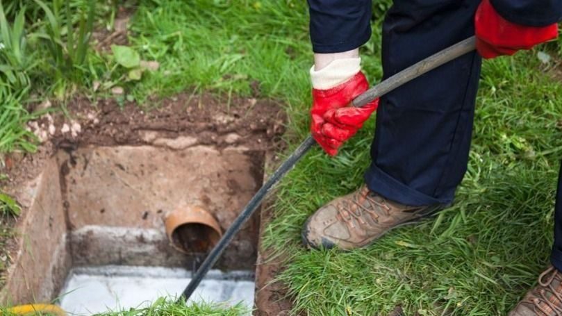 Man with ground open using hydro jetting tool to unclog pipe.
