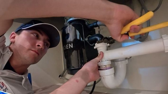 Stuart plumber tightening a pipe under the sink to fit leak.