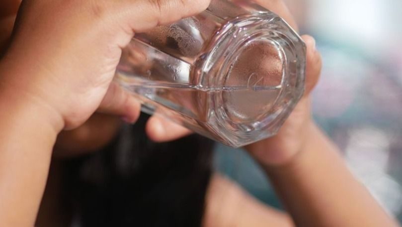 Close-up of hands holding a clear glass bottle and tilting it to drink water.